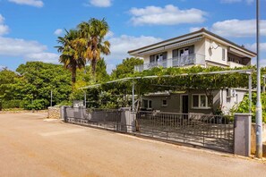 A two-story house with a balcony, a gated entrance, and a palm tree in the background.