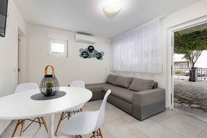 A modern living room with a white round table, white chairs, a grey sofa, and a decorative wall piece.
