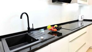 A modern kitchen with a black sink, a stainless steel faucet, a fruit bowl on the counter, and a white kettle.