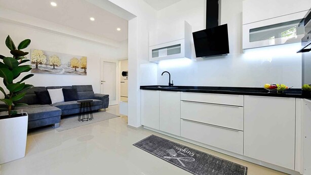 A modern kitchen with white cabinetry, a black countertop, and a flat-screen TV mounted above the sink.