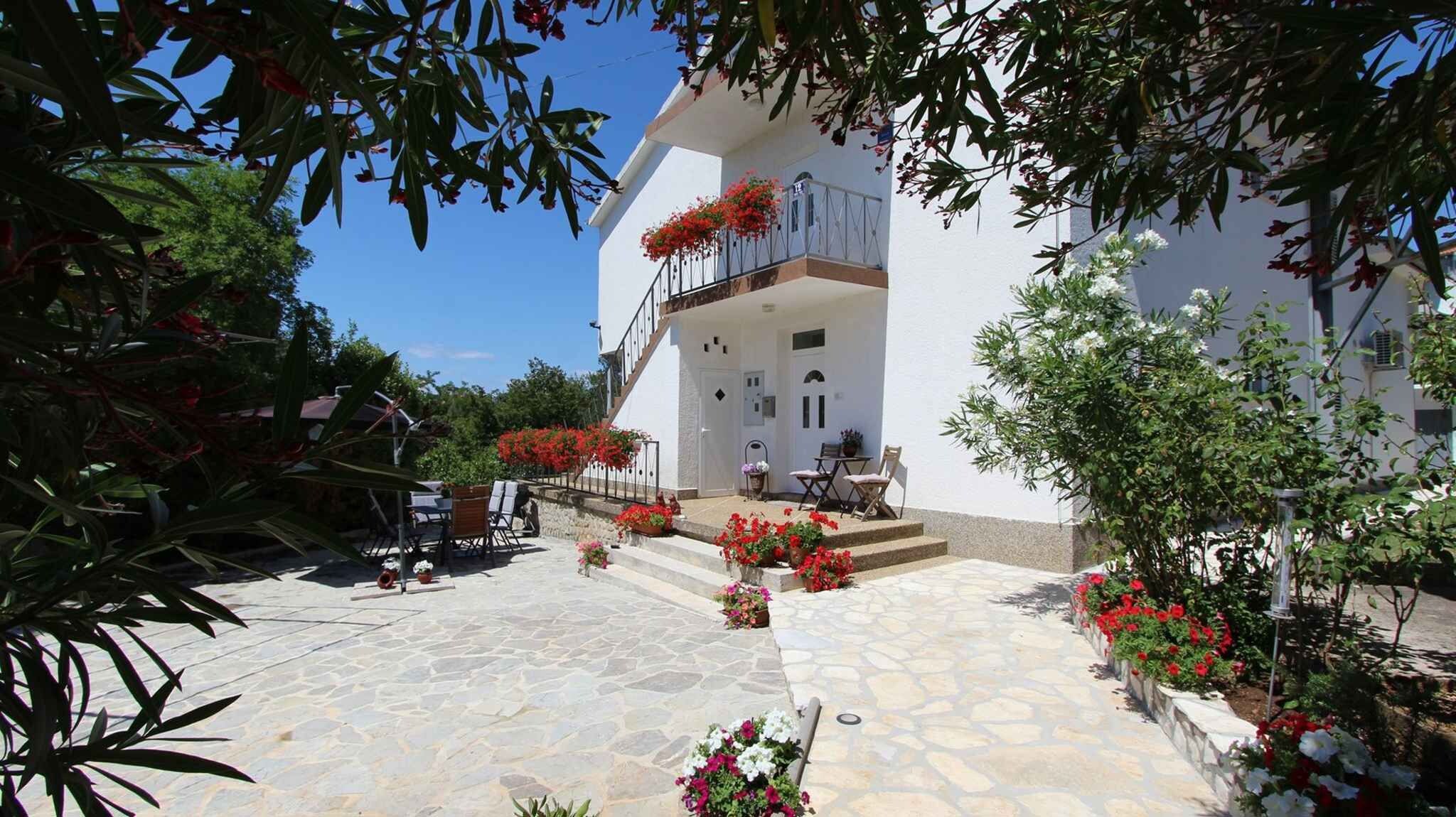 Un edificio blanco con patio de piedra, mesas al aire libre y flores rojas.