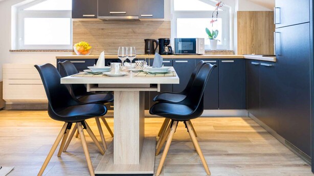 Een moderne keuken met donkere kastjes, een houten eettafel en zwarte stoelen.