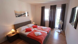 A hotel room with a bed, bedside lamps, a window with curtains, a fan, and a painting on the wall.