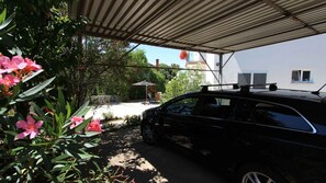 A covered parking area with a car, a patio with a table and chairs, and a house in the background.
