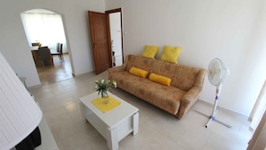 A living room with a sofa, a small table, and a standing fan.