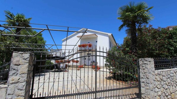 A gated entrance with a white building, a stone wall, and a palm tree.