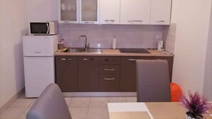 Eine kleine Küche mit weißen Schränken, einer eingebauten Mikrowelle, einem Spülbecken und einem kleinen Kühlschrank.