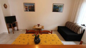 Ein Wohnzimmer mit Esstisch, Stühlen, einer schwarzen Couch und zwei Bildern an der Wand.