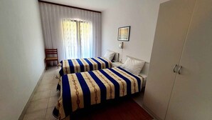 Ein Hotelzimmer mit zwei Betten, einem Sessel, einem Kleiderschrank und einem Fenster mit Vorhängen.