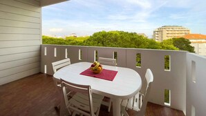A balcony with a white table and chairs, a red placemat, and a bowl of fruit.