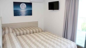 Un dormitorio con una cama, un cuadro de una luna sobre el agua, un televisor y una ventana con cortinas.