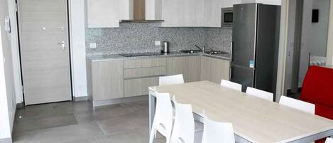 Una cocina moderna con armarios blancos, encimera de granito y refrigerador de acero inoxidable.