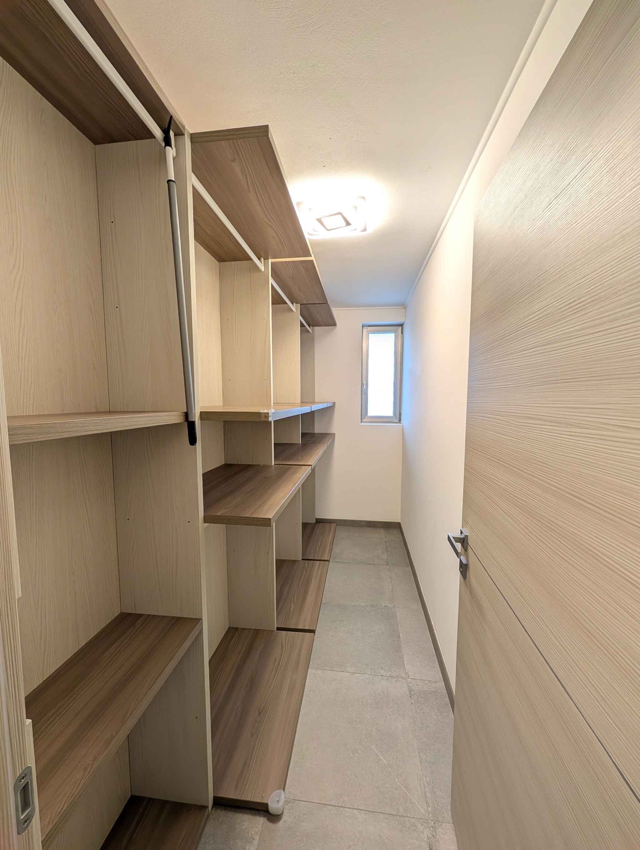 A narrow hallway with wooden shelving units and a door on the right.