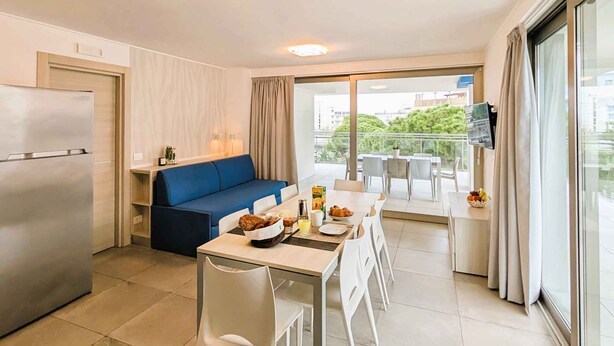 A modern kitchen with a dining area, a blue sofa, and a balcony with a view.