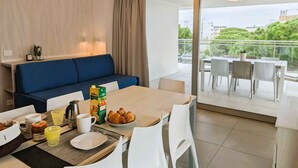 A modern hotel room with a dining area, a blue sofa, breakfast setup, and a balcony with a view.