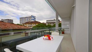 Un balcon avec une table et des chaises blanches, une plante en pot et une vue sur des bâtiments en arrière-plan.