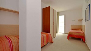 A bedroom with two single beds, a wardrobe, and a window. - Holiday apartment with pool and air conditioning (Lignano)