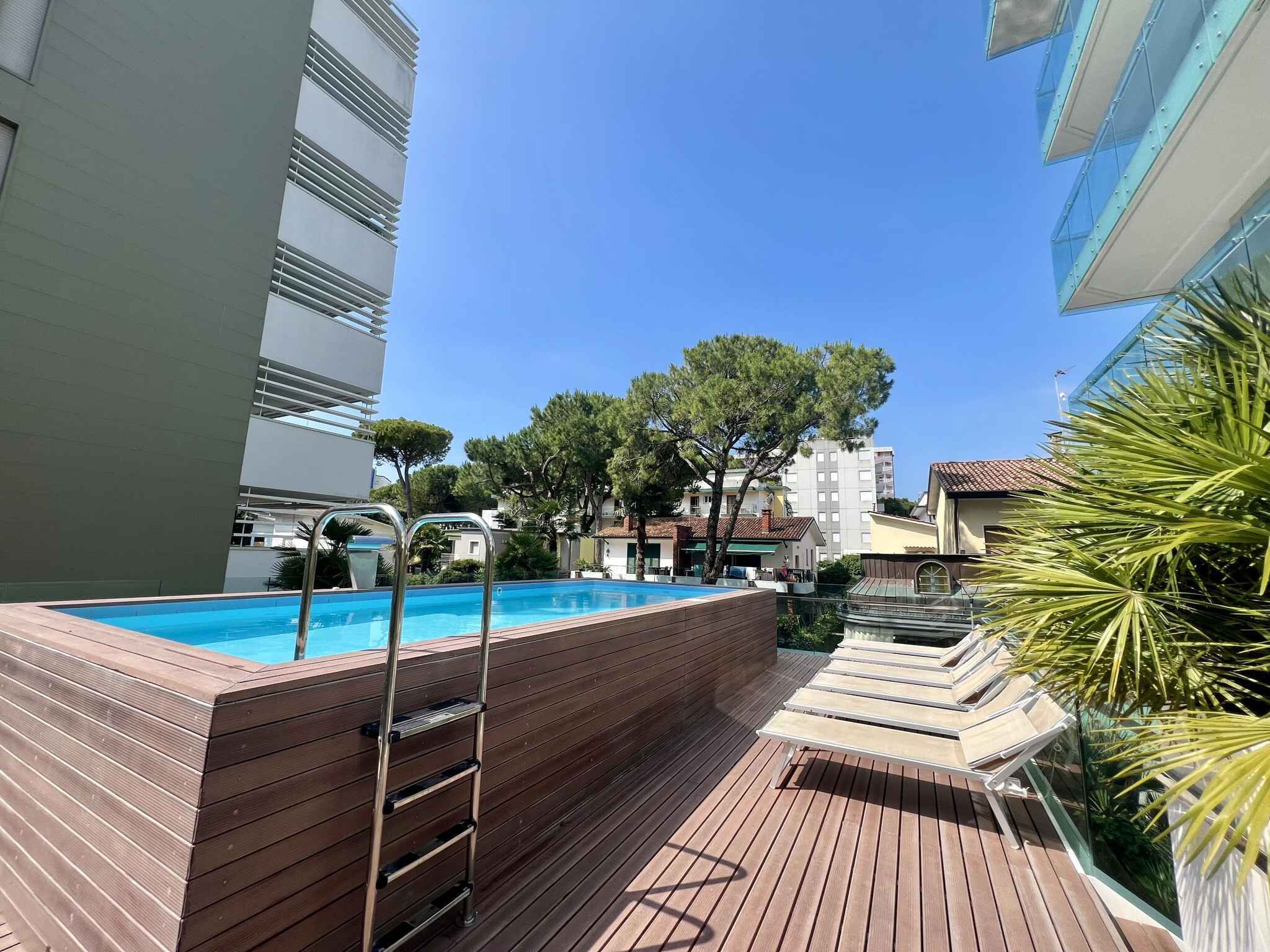 A rooftop pool area with wooden deck, metal pool ladder, and lounge chairs.