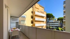 A balcony with a dining area, including a table and chairs, overlooking a yellow building with multiple balconies. - Holiday apartment with pool and air conditioning (Lignano)