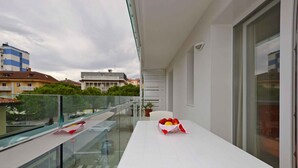 Un balcon avec une table blanche, un panneau de signalisation indiquant un arrêt obligatoire, et une vue sur des immeubles et des arbres.