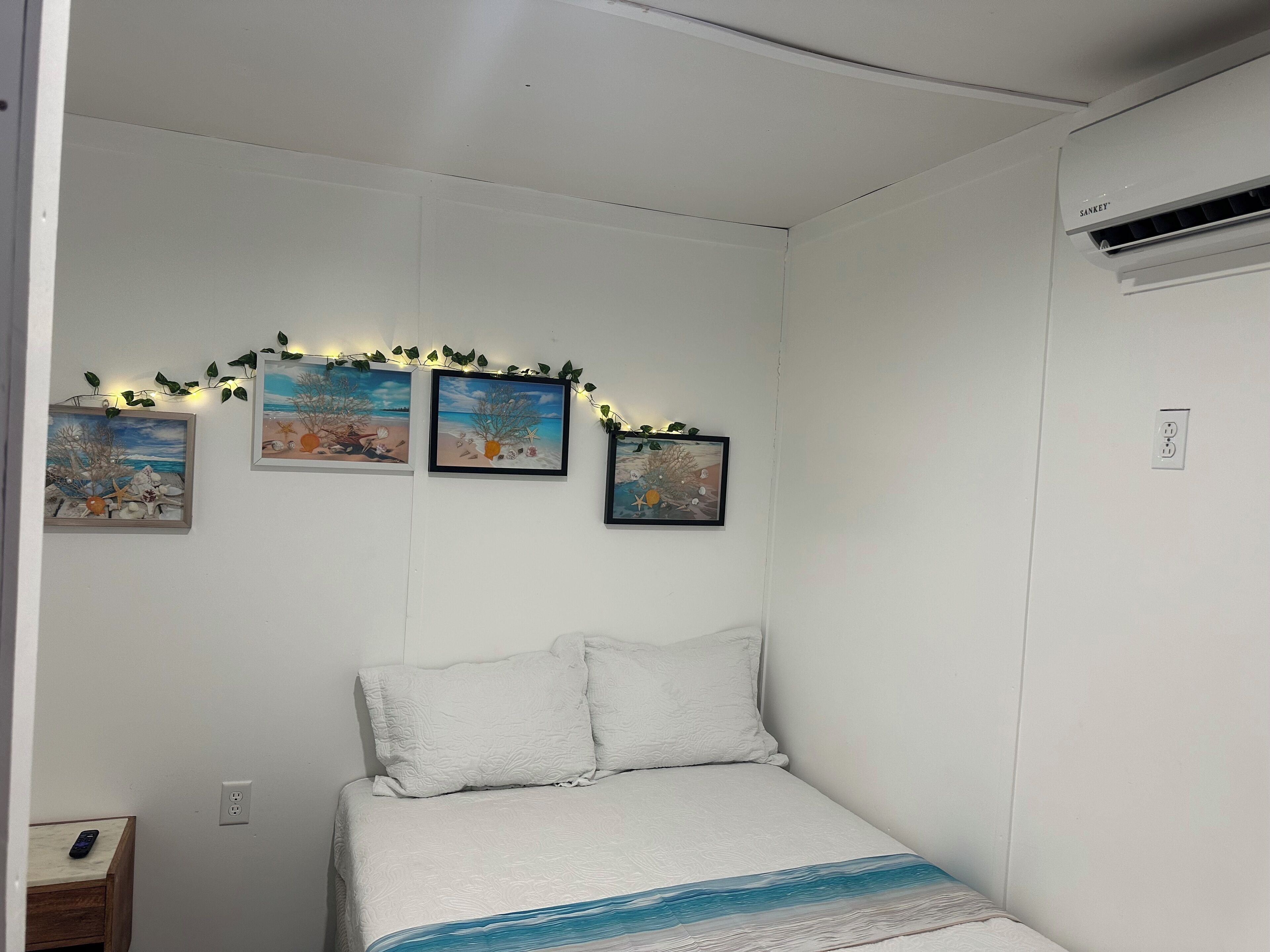 Un dormitori amb un llit, una tauleta de nit i tres quadres al mur.