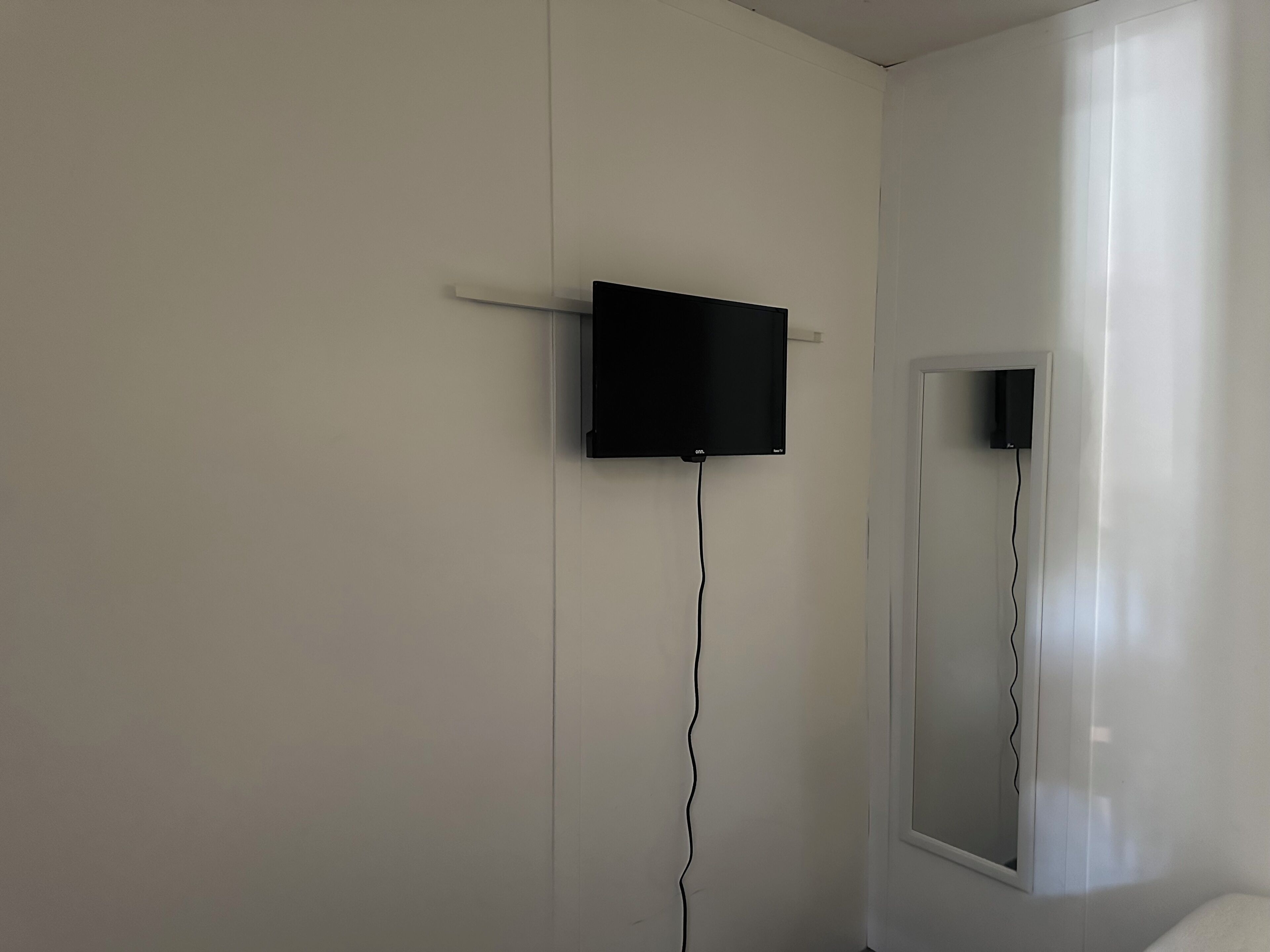 Ein Zimmer mit an der Wand montiertem Flachbildfernseher, einer Tür und einem Fenster.