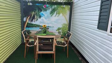 Eine Terrasse mit Tisch und Stühlen, ein Wandgemälde mit Strandmotiv und eine kleine Gartenanlage mit einer Sonnenblume.