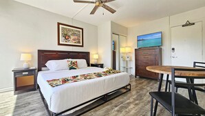 A hotel room with a bed, a desk, a chair, a wardrobe, a ceiling fan, and a painting on the wall. - Comfortable King Bed Waikiki Studio 2 mins walk to Beach with WiFi & AC (Honolulu)