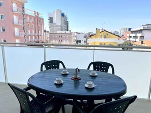 A round table with four chairs and a coffee pot on a balcony with a city view.