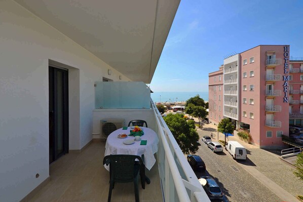A balcony with a table set for dining, overlooking a street with parked cars and a building labeled "HOTEL MARIN".