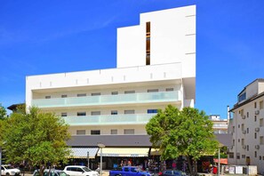 A multi-story building with a modern design, featuring a prominent vertical element and a ground-level shop with a striped awning.