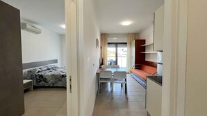 Un pasillo estrecho que conduce a un dormitorio con cama, una pequeña kitchenette y un comedor con mesa y sillas.