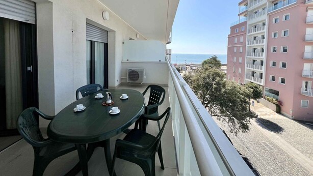 Un balcón con mesa y sillas, con vistas a una zona costera con edificios y cielo despejado.