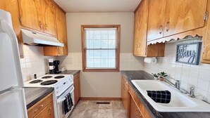 A compact kitchen with wooden cabinets, a stove, oven, sink, and a window with blinds. - 146 Wedgewood Wonder - Charming 2 bed 1 bath (Lincoln)