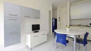 Una cocina moderna con armarios blancos, una mesa de comedor con sillas azules y un televisor sobre un mueble blanco.