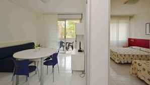 Una habitación con una mesa blanca, sillas azules, una cama roja y un escritorio blanco con un ordenador.