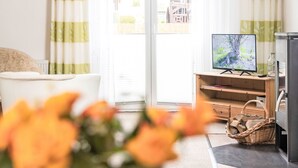 Un salon avec un canapé, un téléviseur posé sur un meuble en bois et une fenêtre avec des rideaux.
