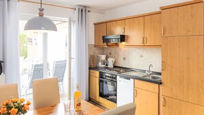A modern kitchen with wooden cabinets, a black microwave, and a dining area with a wooden table and chairs. - Morgensonne by Interhome (Karlshagen)