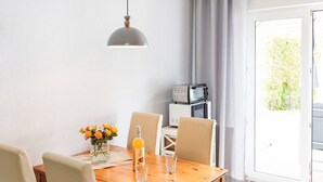 A dining area with a wooden table, beige chairs, a vase with flowers, a bottle, and a glass. There is a microwave on a shelf behind the table. - Morgensonne by Interhome (Karlshagen)