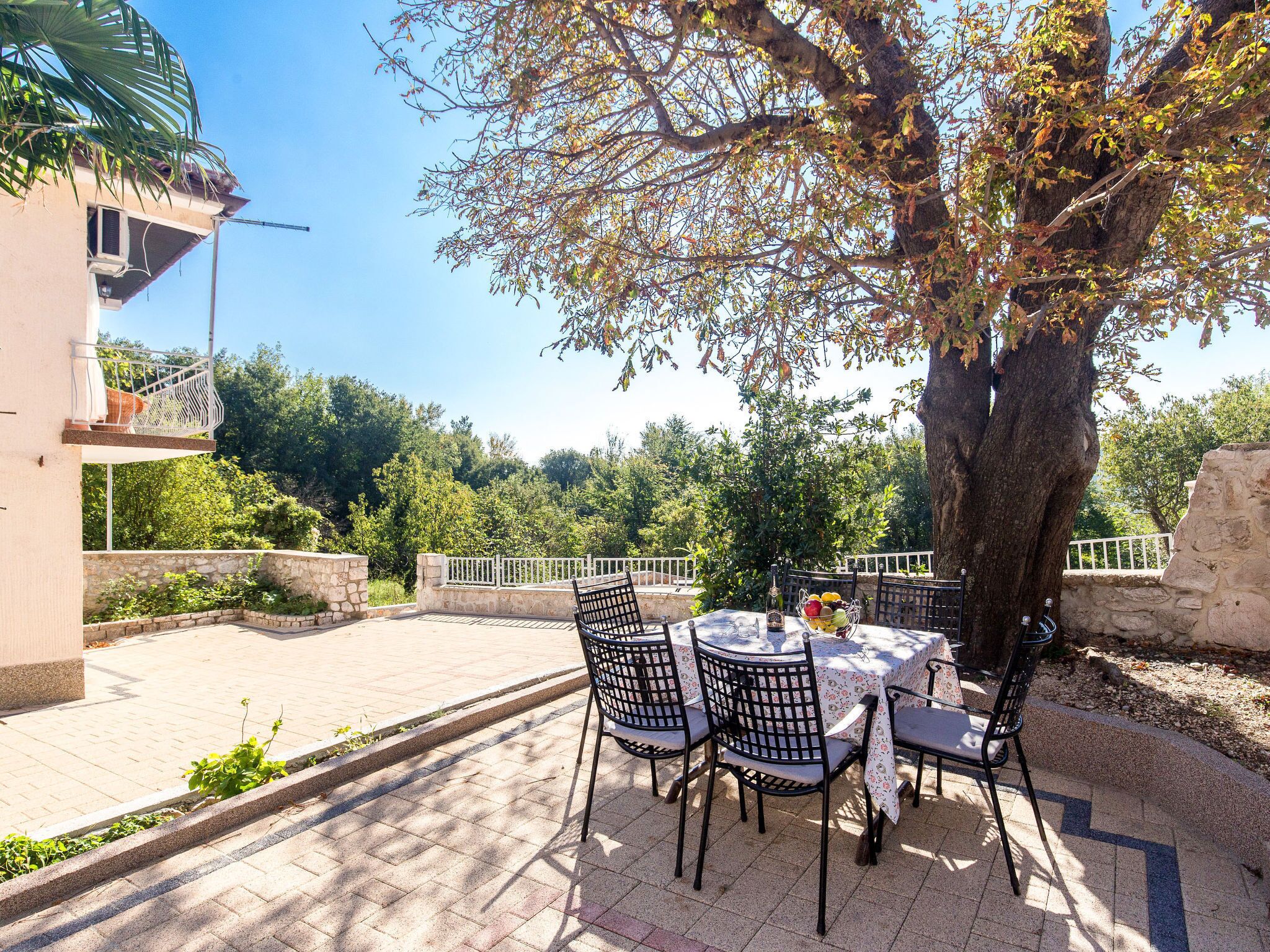 Une terrasse extérieure avec une table ronde et des chaises, entourée de murs en pierre et d’un arbre.