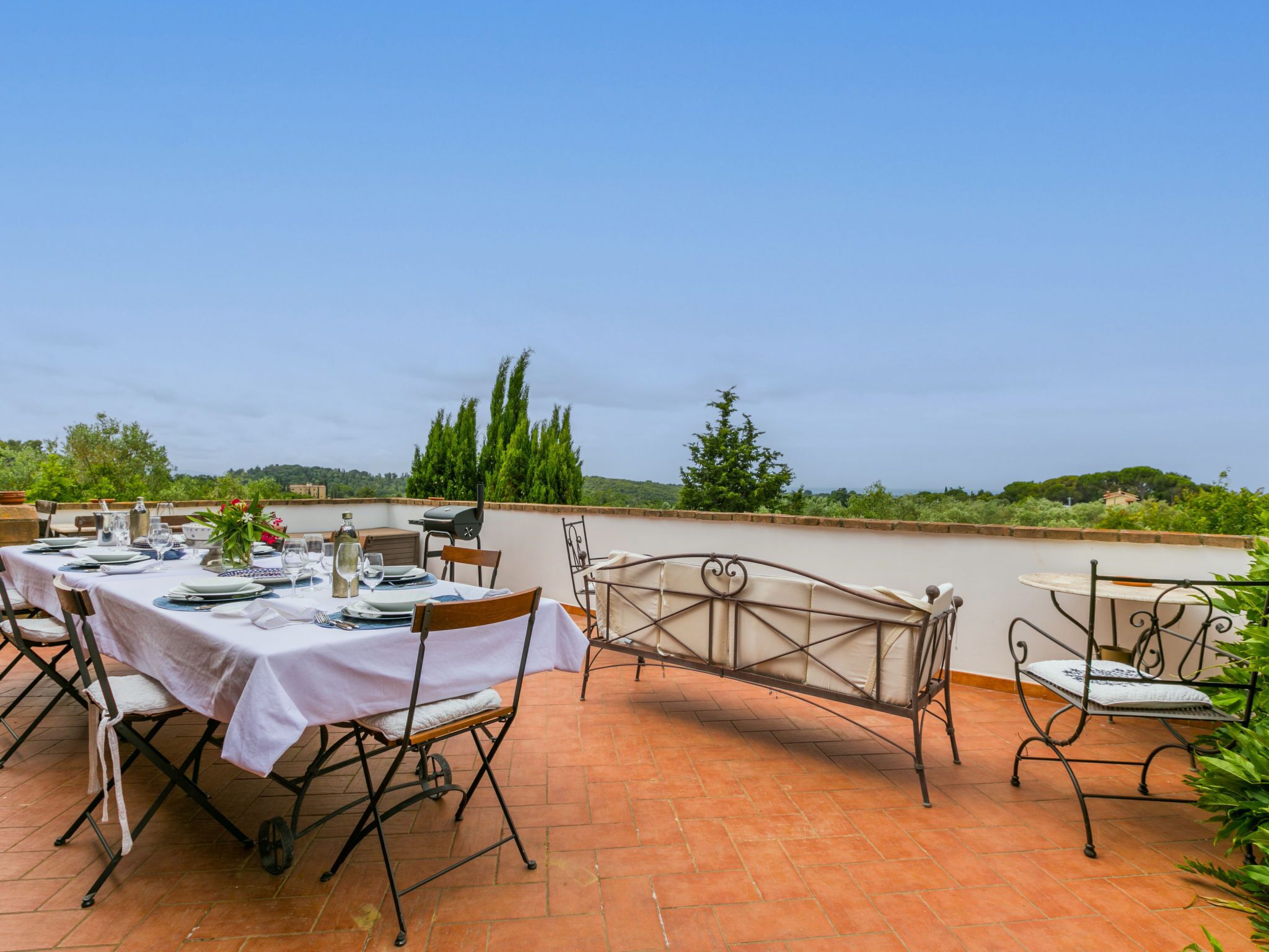 An outdoor dining area with a terrace, tables set for dining, and a view of the countryside.
