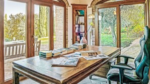 A room with a wooden desk, books, a lamp, and a chair. There are large windows with a view of greenery outside. - Tramonto by Interhome (Guardistallo)
