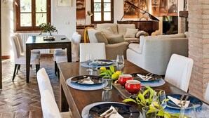 A dining area with a long table set for six, flanked by white chairs, under a brick archway. - Tramonto by Interhome (Guardistallo)