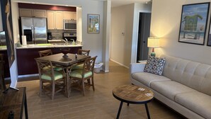 A modern living room with a beige sofa, a small round coffee table, and a dining area with a wooden table and chairs. - "Nothing But Sunshine" (Fort Myers)