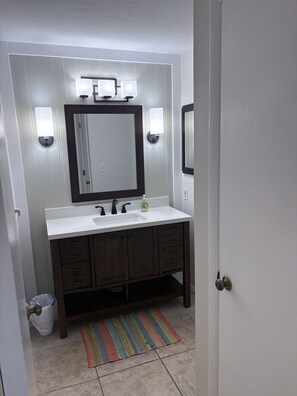 A bathroom with a white vanity, dark wooden cabinets, a large mirror, and two wall-mounted lights. - "Nothing But Sunshine" (Fort Myers)