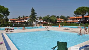Uma área de piscina com espreguiçadeiras e um edifício com telhados vermelhos ao fundo.