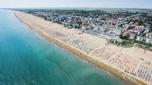 Eine Luftaufnahme einer Küstenstadt mit einem langen Strand, gesäumt von Reihen aus Strandstühlen und Sonnenschirmen.