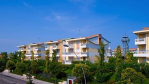 Eine Reihe moderner Apartmenthäuser mit Balkonen, umgeben von üppigem Grün und blauem Himmel.