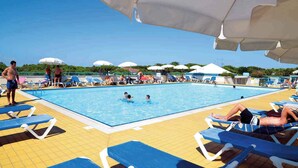 Un espace piscine agrémenté de chaises longues et de parasols, entouré de verdure.