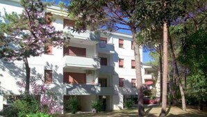Un edificio de varios pisos con balcones, rodeado de árboles y vegetación.
